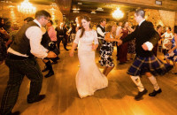 A bride and a guest in a kilt dancing a ceilidh with wedding guests at a Scottish wedding reception